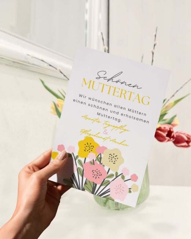 Hand hält eine Muttertagskarte von Avantis Tagespflege und Pflegedienst Aachen mit Blumenmotiv.
